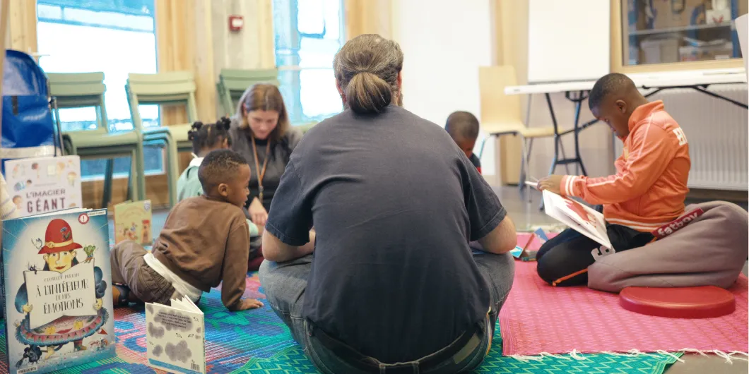 Un groupe d’enfants participe à un atelier de lecture avec 2 travailleurs sociaux à la Maison des réfugié·es.